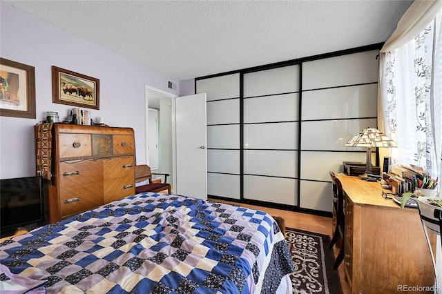 bedroom with visible vents, a textured ceiling, and wood finished floors