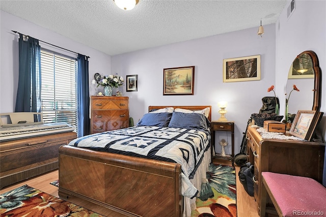 bedroom featuring visible vents, a textured ceiling, and wood finished floors