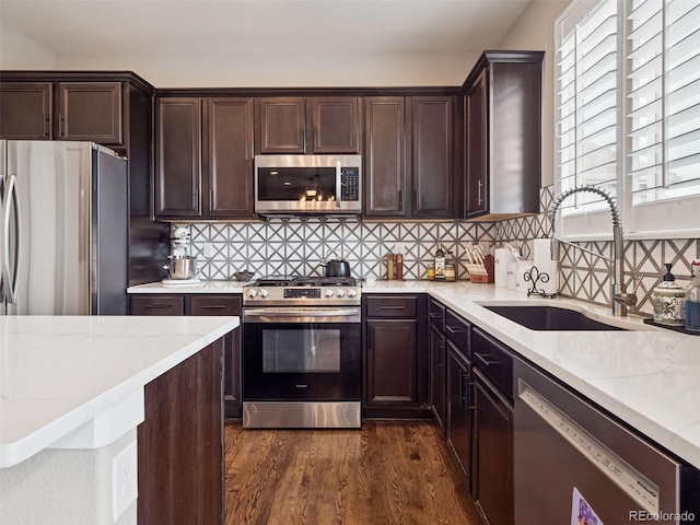 kitchen with backsplash, light stone countertops, a sink, dark wood-style floors, and stainless steel appliances