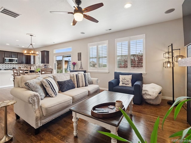 living area featuring ceiling fan with notable chandelier, dark wood-style floors, and visible vents