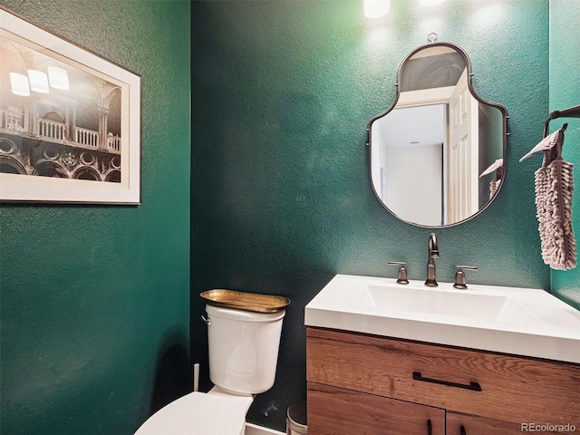 bathroom featuring toilet, a textured wall, and vanity
