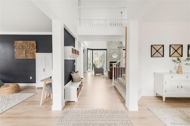 foyer entrance featuring crown molding, a high ceiling, light wood finished floors, stairs, and baseboards