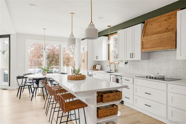 kitchen with decorative backsplash, a kitchen bar, a sink, light countertops, and black electric stovetop