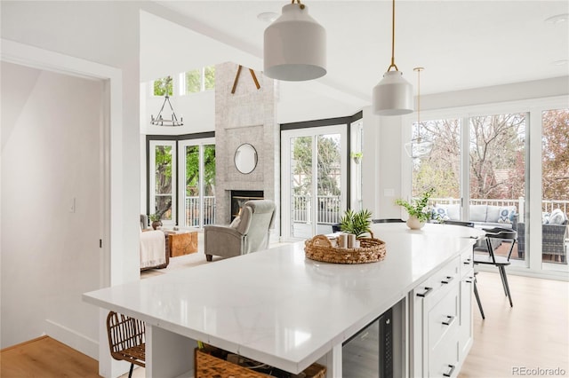 kitchen featuring beverage cooler, light wood-style floors, light countertops, white cabinets, and hanging light fixtures