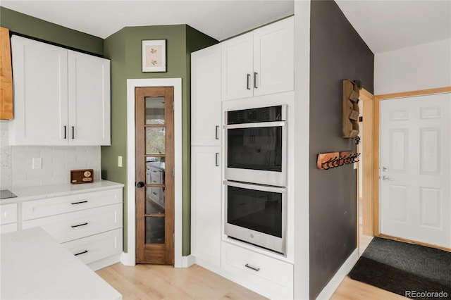 kitchen featuring tasteful backsplash, light countertops, light wood finished floors, double wall oven, and white cabinetry