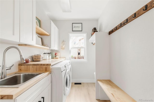 laundry room featuring washing machine and clothes dryer, cabinet space, a sink, light wood-style flooring, and baseboards