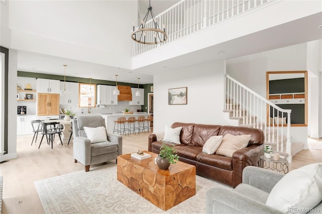 living room with light wood-type flooring, a towering ceiling, stairway, and an inviting chandelier