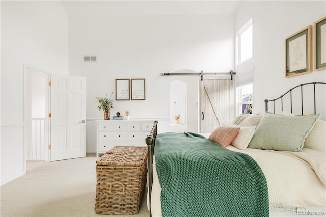 bedroom with a barn door, a towering ceiling, carpet floors, and visible vents