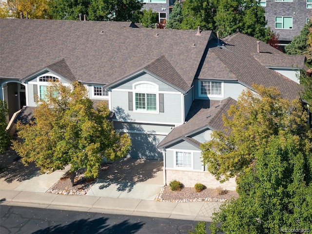view of front of property with concrete driveway, an attached garage, a shingled roof, and brick siding