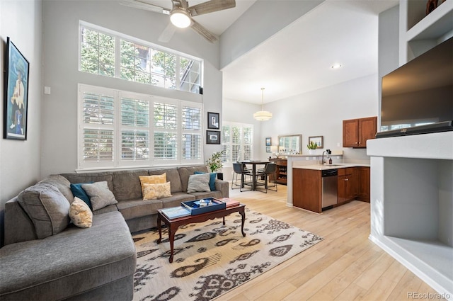living area with a high ceiling, ceiling fan, and light wood-style flooring