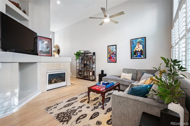 living area with high vaulted ceiling, ceiling fan, wood finished floors, and a tile fireplace