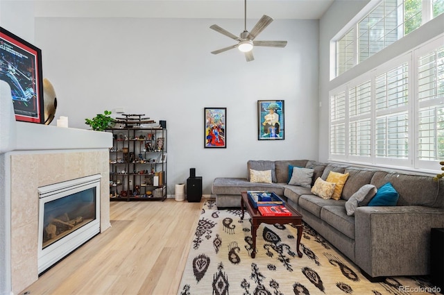 living area with healthy amount of natural light, a towering ceiling, wood finished floors, a ceiling fan, and a fireplace