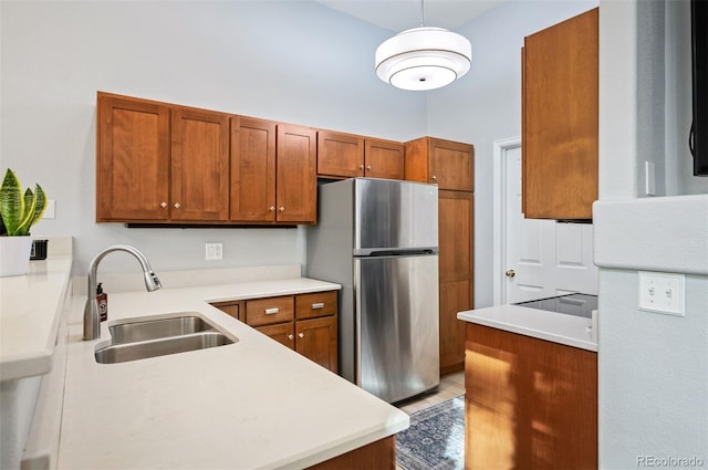 kitchen featuring freestanding refrigerator, a sink, brown cabinets, light countertops, and hanging light fixtures