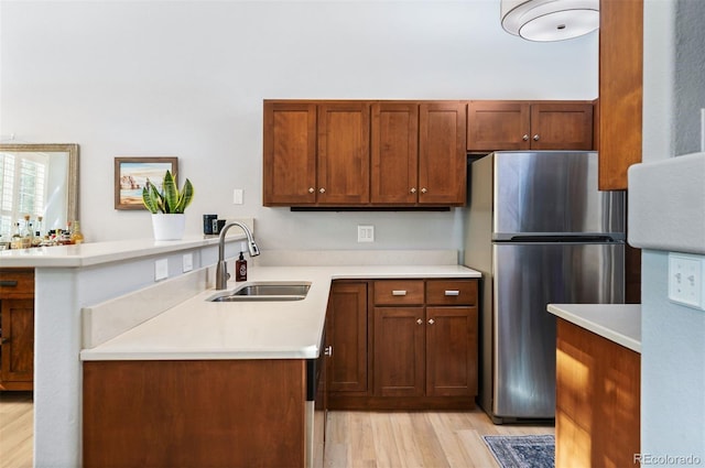kitchen with freestanding refrigerator, a sink, a peninsula, light wood-style floors, and light countertops