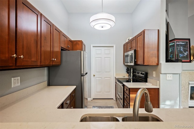 kitchen with appliances with stainless steel finishes, a sink, light wood-style flooring, and hanging light fixtures