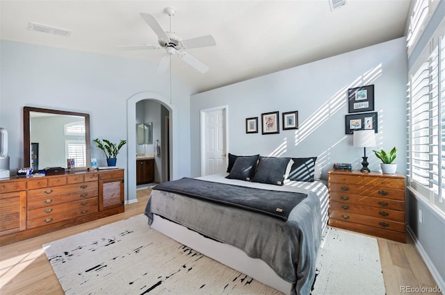 bedroom featuring light wood finished floors, multiple windows, arched walkways, lofted ceiling, and connected bathroom