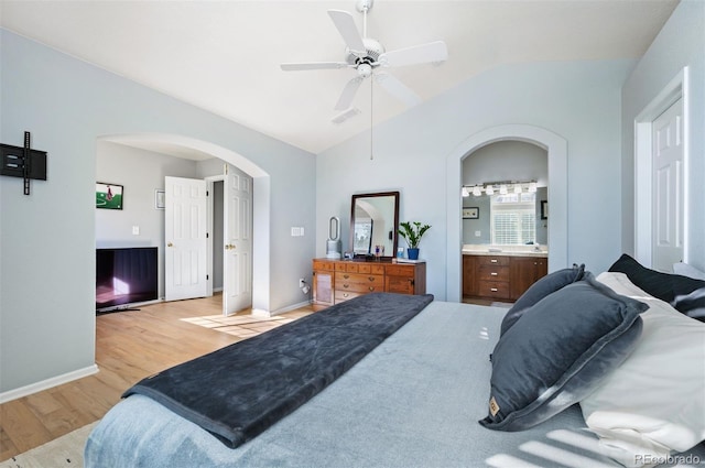 bedroom with arched walkways, light wood-style flooring, vaulted ceiling, ensuite bathroom, and a ceiling fan