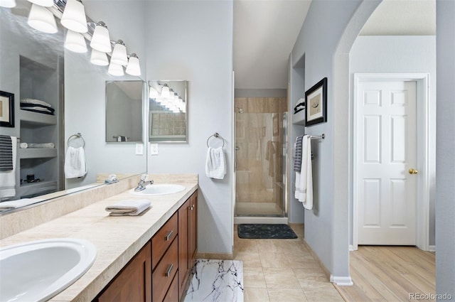 full bath with a stall shower, double vanity, and baseboards