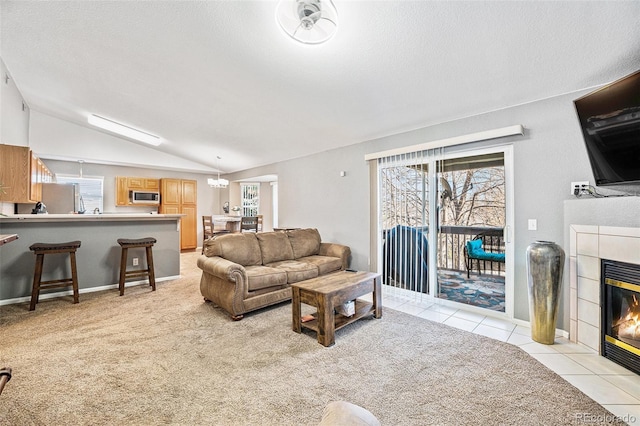 living area with a textured ceiling, light tile patterned floors, lofted ceiling, light colored carpet, and a tile fireplace