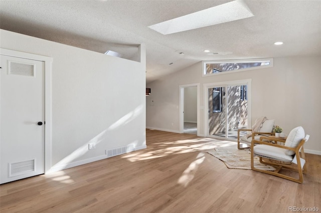 sitting room featuring lofted ceiling with skylight, light hardwood / wood-style floors, and a textured ceiling