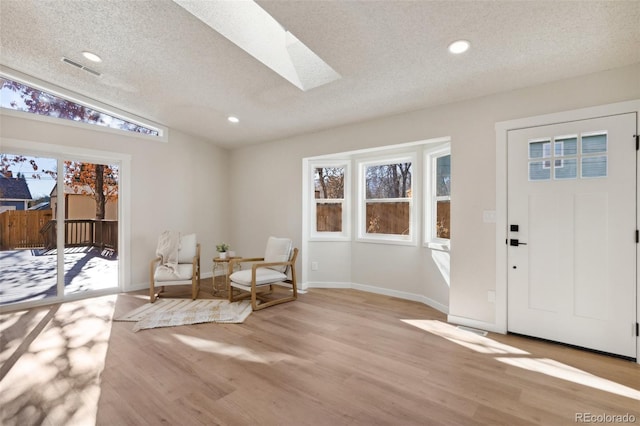 entryway with a textured ceiling, light wood-type flooring, plenty of natural light, and vaulted ceiling with skylight