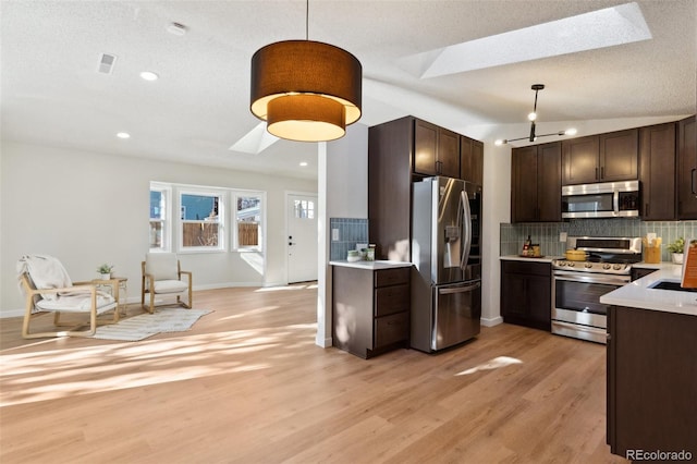 kitchen featuring lofted ceiling with skylight, stainless steel appliances, decorative light fixtures, and light hardwood / wood-style floors