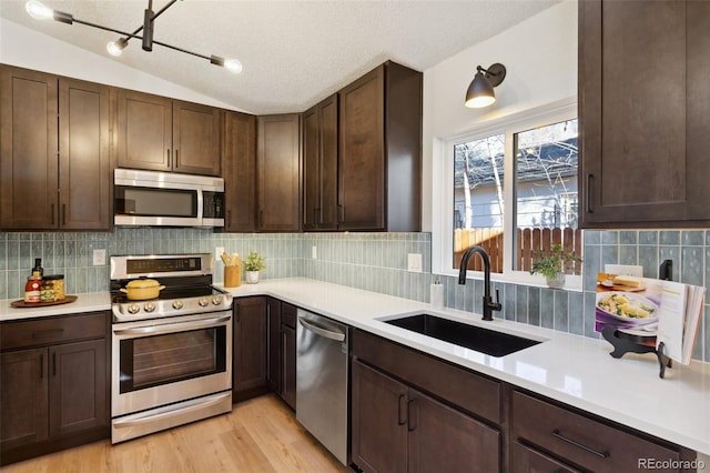 kitchen with decorative backsplash, appliances with stainless steel finishes, a textured ceiling, sink, and lofted ceiling