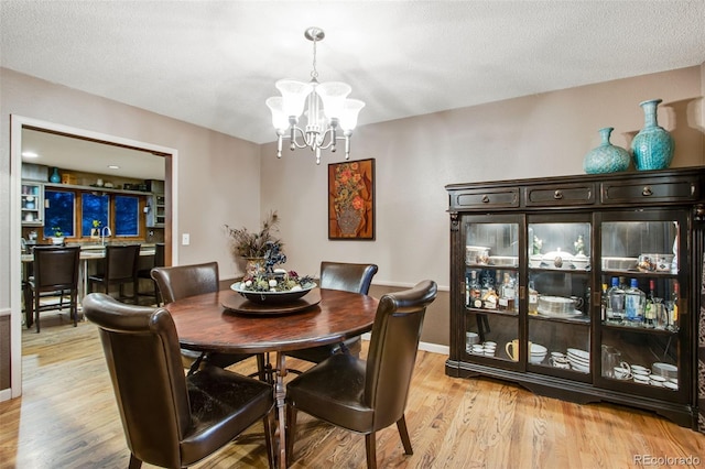 dining space featuring sink, light hardwood / wood-style floors, a textured ceiling, and a notable chandelier