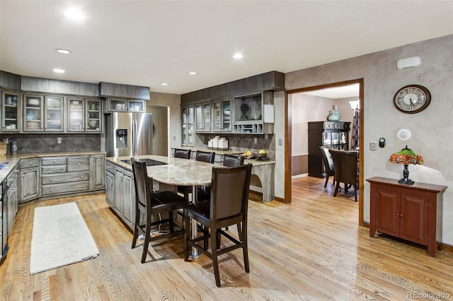 kitchen featuring a kitchen breakfast bar, a center island, stainless steel fridge with ice dispenser, light stone countertops, and light wood-type flooring