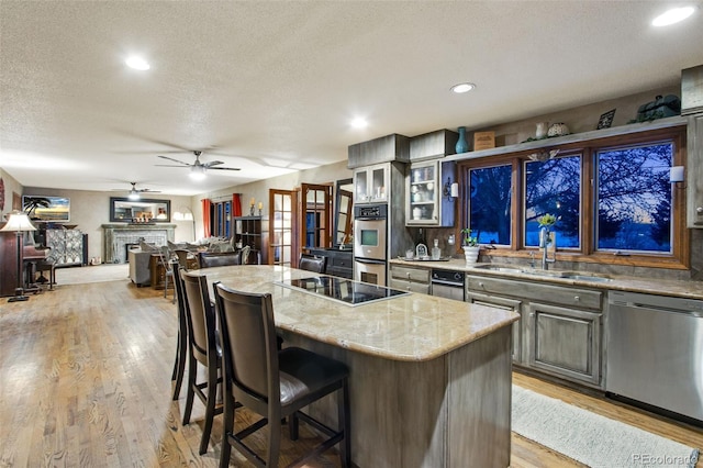 kitchen with a kitchen island, appliances with stainless steel finishes, sink, light stone counters, and light wood-type flooring