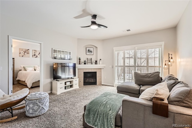 living room featuring ceiling fan, a tile fireplace, carpet flooring, and baseboards