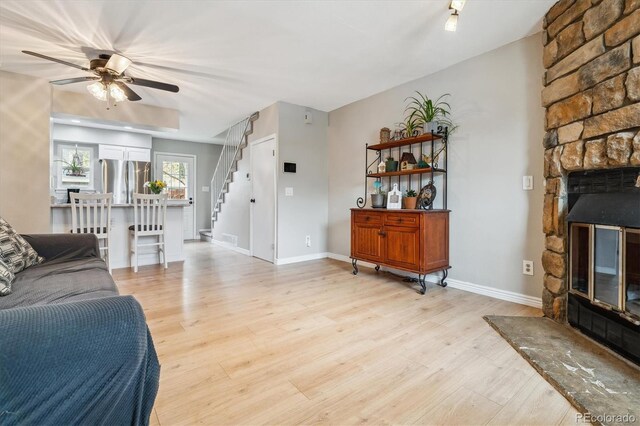 living area with baseboards, light wood-type flooring, a ceiling fan, and stairs