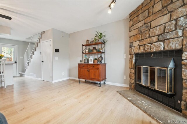 living room featuring ceiling fan, a large fireplace, baseboards, stairs, and light wood-style flooring
