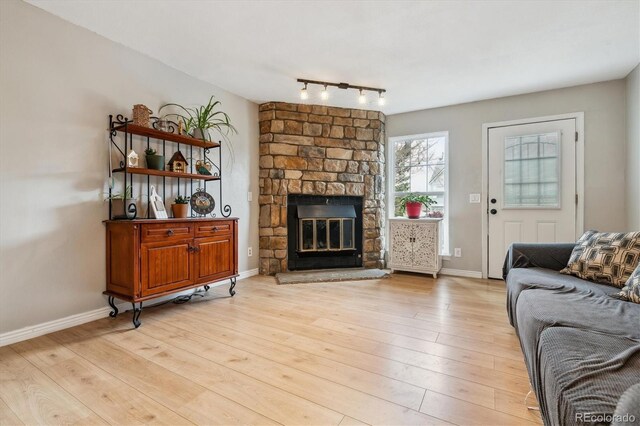 living area featuring a stone fireplace, rail lighting, light wood finished floors, and baseboards