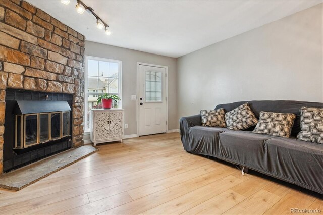 living area featuring track lighting, a large fireplace, baseboards, and wood finished floors