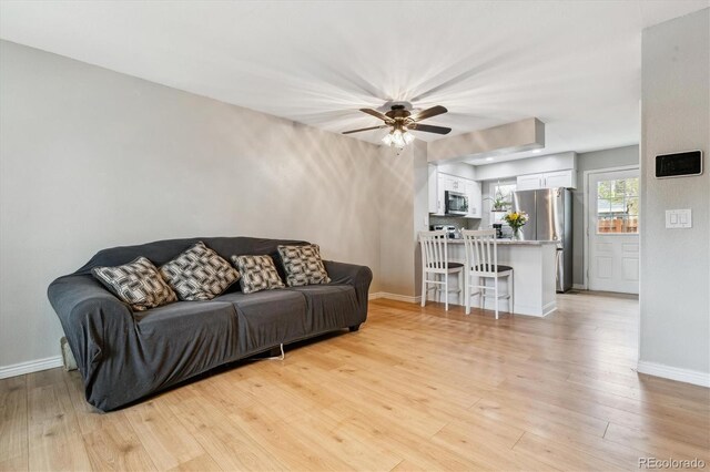 living room featuring a ceiling fan, baseboards, and light wood finished floors