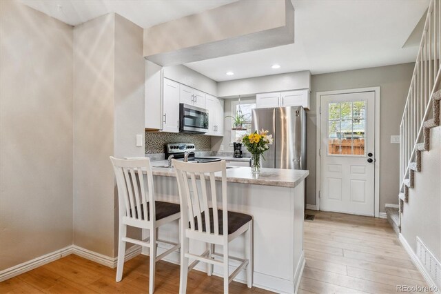 kitchen with light wood-type flooring, light countertops, a peninsula, stainless steel appliances, and white cabinetry