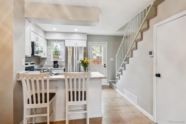 kitchen featuring visible vents, a peninsula, white cabinets, light wood-style flooring, and stainless steel appliances