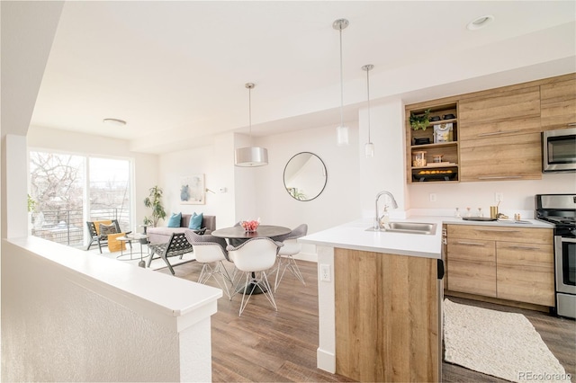 kitchen featuring stainless steel appliances, a kitchen island with sink, sink, wood-type flooring, and pendant lighting