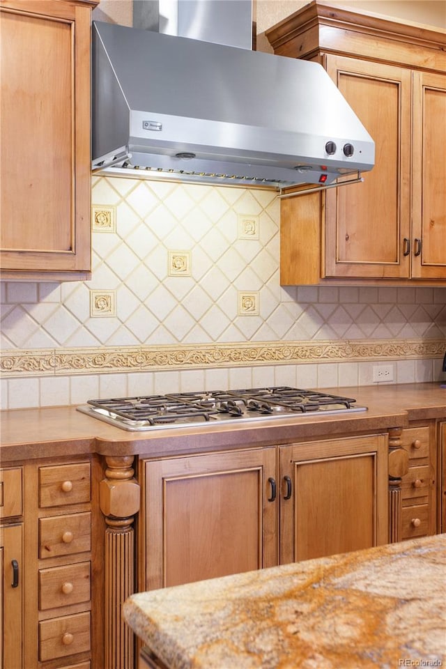 kitchen with light stone counters, decorative backsplash, wall chimney exhaust hood, and stainless steel gas stovetop