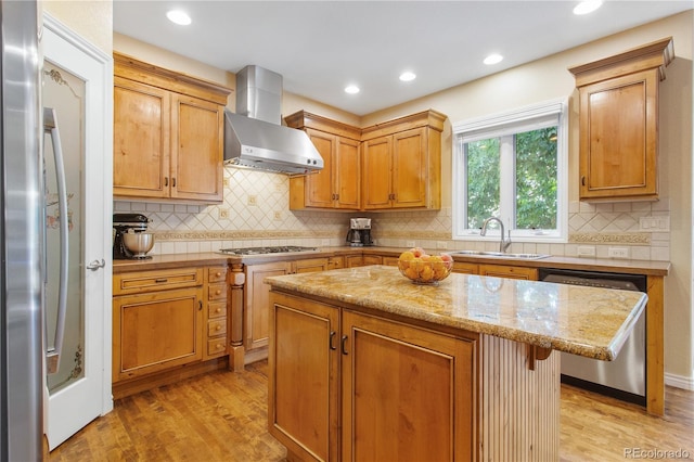 kitchen featuring a sink, stainless steel appliances, light wood-style floors, wall chimney range hood, and a center island