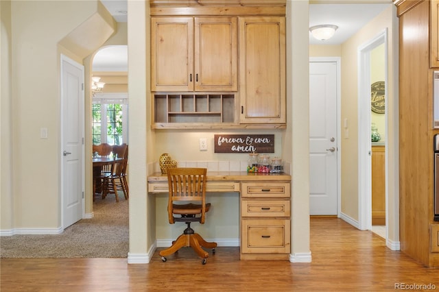 home office featuring baseboards, arched walkways, light wood-style floors, and built in desk