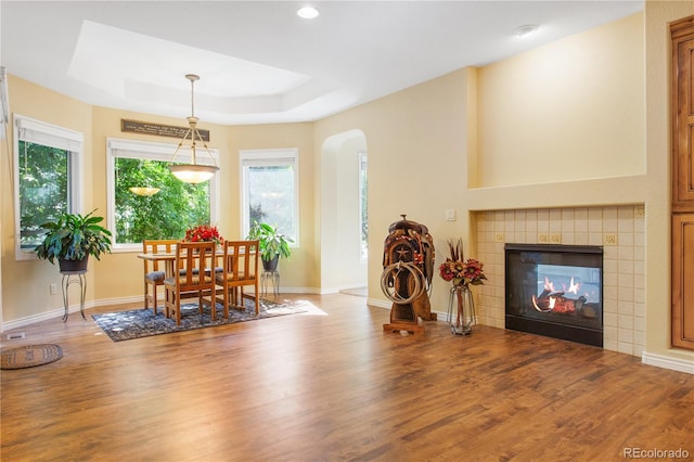 dining space featuring a raised ceiling, wood finished floors, arched walkways, a fireplace, and baseboards