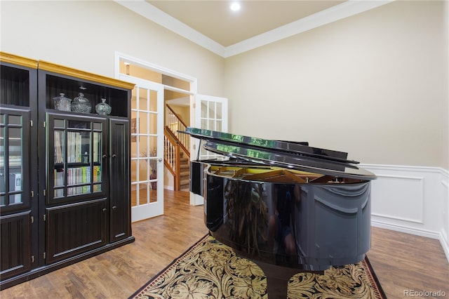 interior space with a wainscoted wall, ornamental molding, french doors, wood finished floors, and a decorative wall