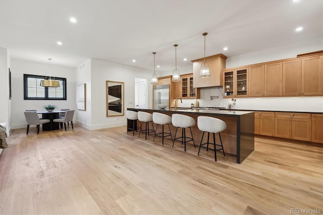 kitchen featuring a kitchen breakfast bar, stainless steel built in refrigerator, sink, decorative light fixtures, and an island with sink