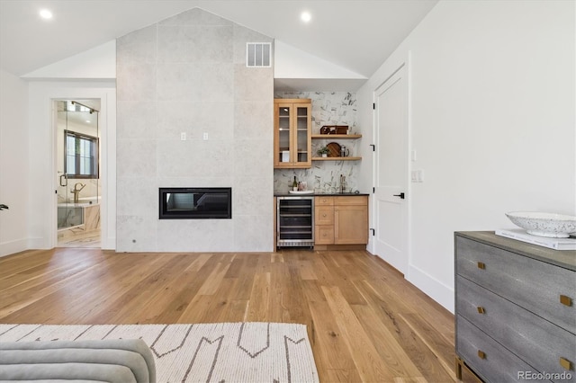 bar featuring light hardwood / wood-style floors, vaulted ceiling, a tile fireplace, and wine cooler