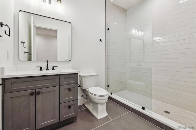 bathroom with vanity, toilet, a tile shower, and tile patterned flooring