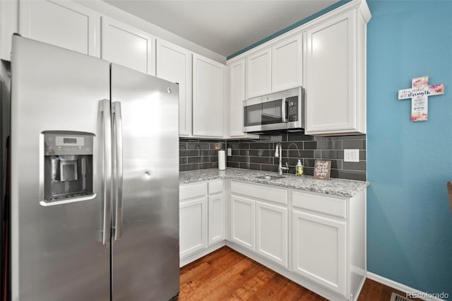 kitchen featuring hardwood / wood-style floors, stainless steel appliances, white cabinetry, sink, and decorative backsplash