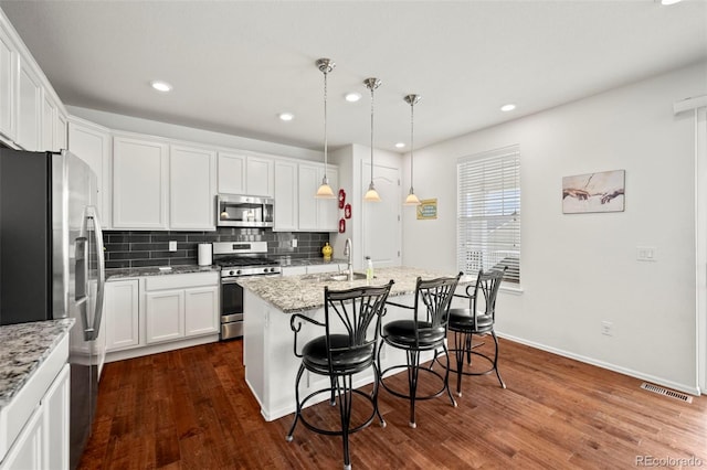 kitchen featuring appliances with stainless steel finishes, white cabinetry, dark hardwood / wood-style floors, a center island with sink, and tasteful backsplash