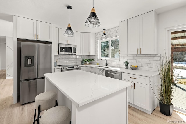 kitchen with light hardwood / wood-style floors, appliances with stainless steel finishes, a kitchen island, pendant lighting, and white cabinets